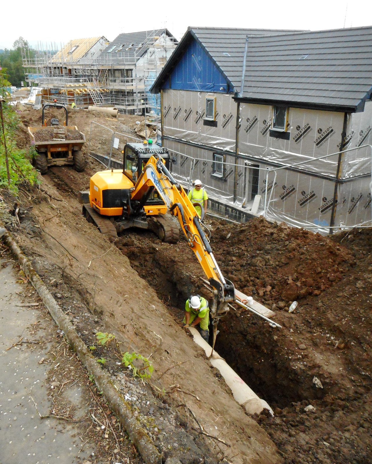 Excavator laying a drainage run in an open trench on a construction site